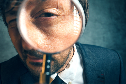 Enlarged eye of tax inspector looking through magnifying glass, inspecting offshore company financial papers, documents and reports.